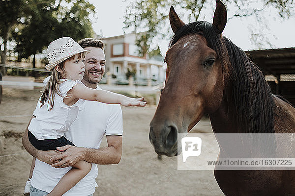 Vater  der seine Tochter trägt und dabei ein Pferd berührt  während er im Freien steht