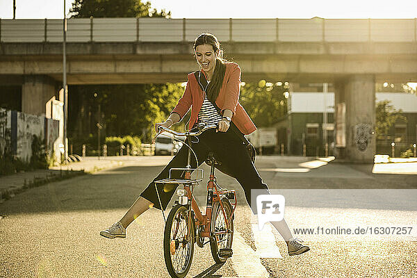 Cheerful young woman enjoying cycling on street during sunny day