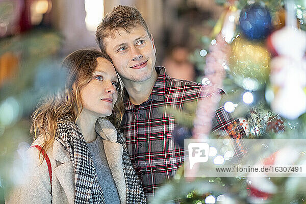 Verliebtes junges Paar mit Blick auf Weihnachtsbaum und Lichter in der Stadt