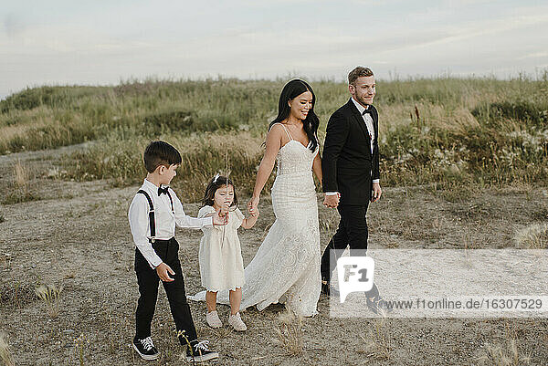 Eltern mit Kindern im Hochzeitskleid beim Spaziergang im Feld