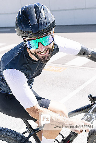Nahaufnahme eines lächelnden amputierten Sportlers mit Sonnenbrille beim Fahrradfahren auf der Straße
