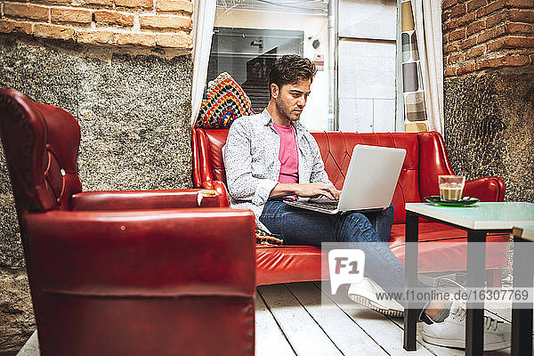 Mittlerer erwachsener Mann  der einen Laptop benutzt  während er auf dem Sofa in einem Café sitzt