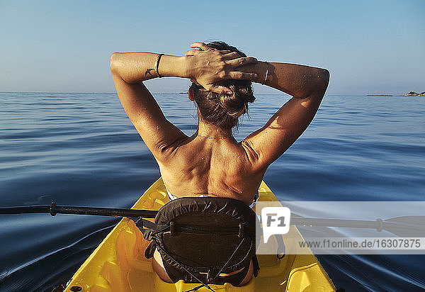 Frau mit Händen hinter dem Kopf sitzt in Boot gegen klaren blauen Himmel