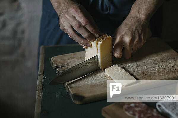 Hände eines Mannes  der handwerklich hergestellte Käsescheiben auf einem Brett am Tisch schneidet