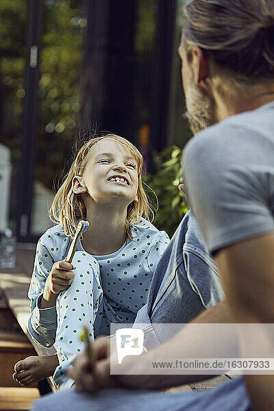 Mädchen zeigt dem Vater die Zähne  während sie mit ihm im Garten putzt