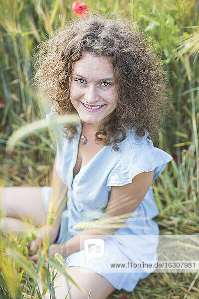Schöne Frau lächelt  während sie in einem landwirtschaftlichen Feld sitzt