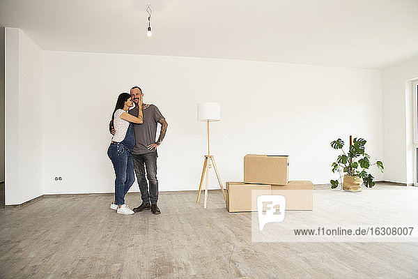 Romantic couple standing by electric lamp and boxes standing against wall in new apartment