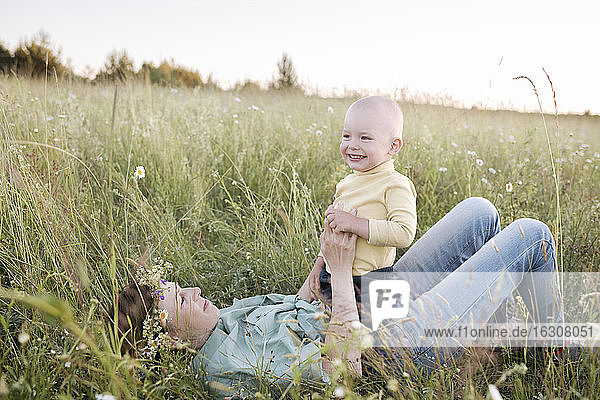 Happy boy sitting on mother lying in grassy field during sunny day