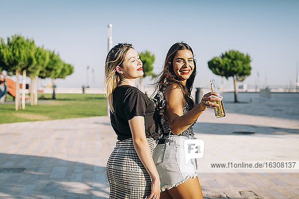 Smiling female friends standing on footpath against clear sky in park