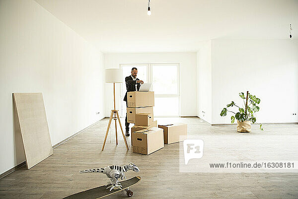 Businessman using laptop on box while standing in new unfurnished apartment