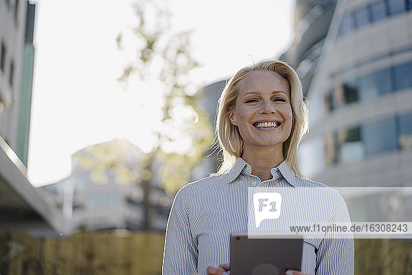 Glückliche blonde Geschäftsfrau mit digitalem Tablet im Finanzviertel der Stadt