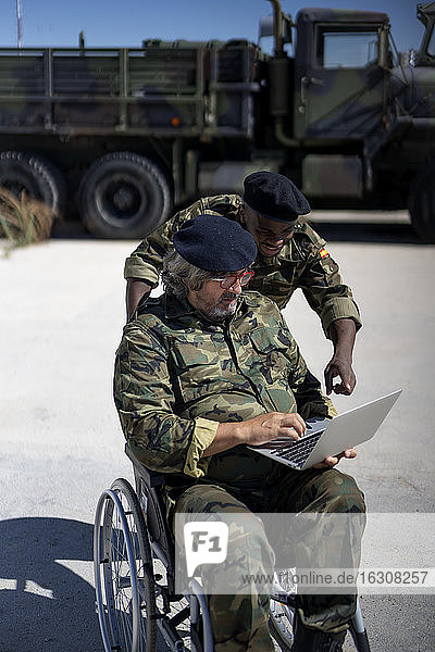 Disabled military officer working on laptop with coworker during sunny day