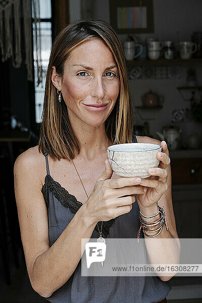 Beautiful woman holding bowl of matcha tea while smiling at cafe