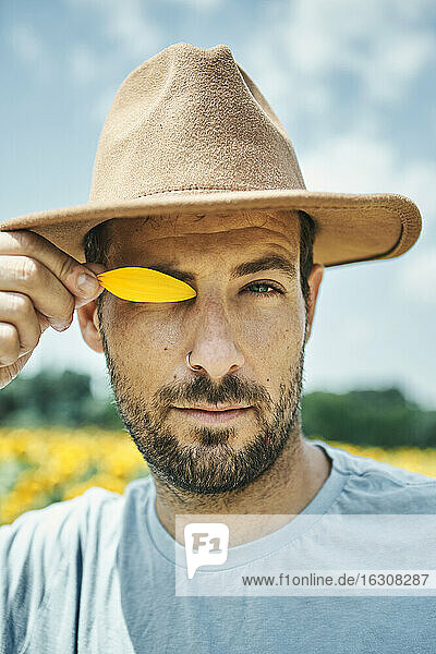 Mann bedeckt Auge mit gelbem Blütenblatt auf einem Feld im Sommer