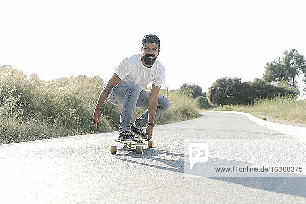 Gutaussehender Mann fährt Skateboard auf der Straße gegen den klaren Himmel