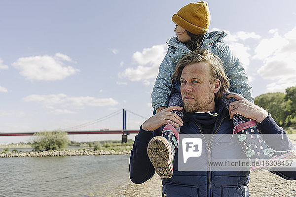 Father carrying daughter on shoulder against river Rhine
