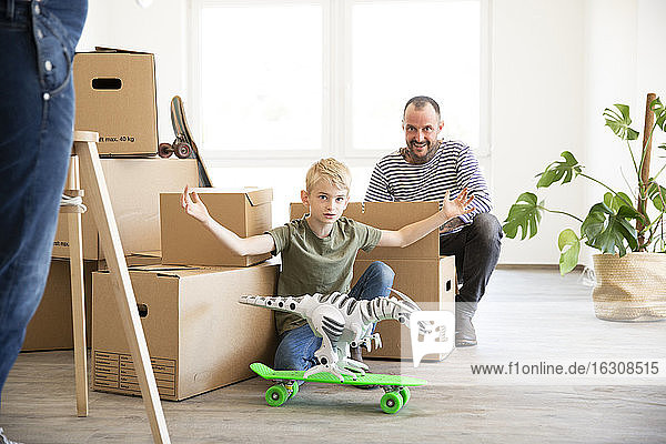 Mann packt Kartons aus  während sein Sohn in der neuen Wohnung mit Spielzeug spielt