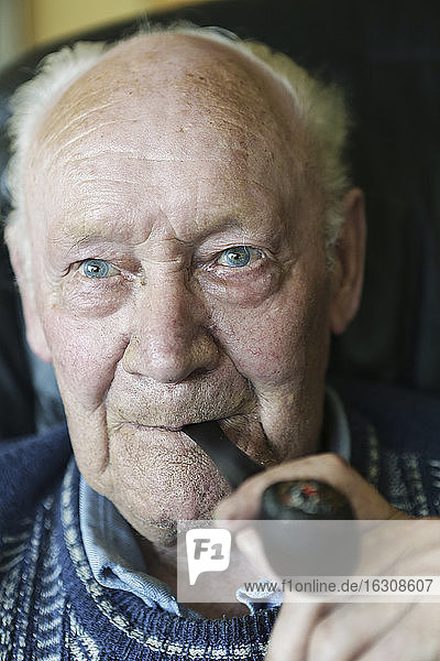 Germany  Portrait of senior man holding pipe  close up