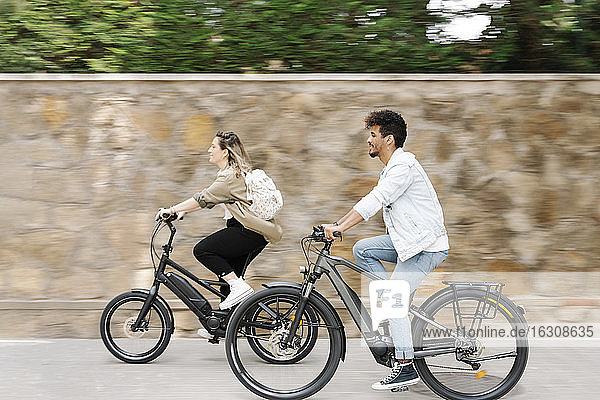 Couple riding electric bicycles on road in city