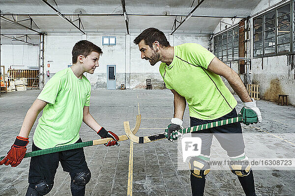Father and son holding hockey sticks while standing face to face while playing on court