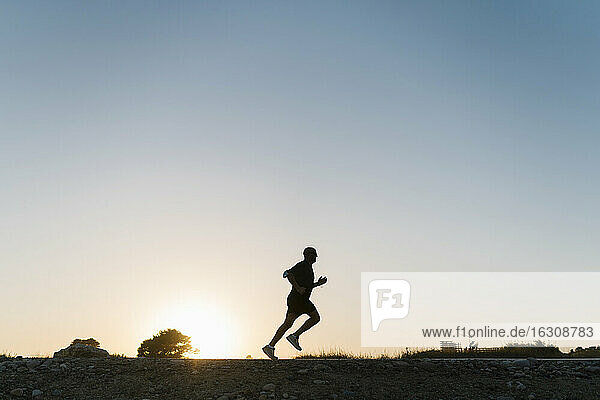 Silhouette of senior athlete jogging against clear sky during sunset