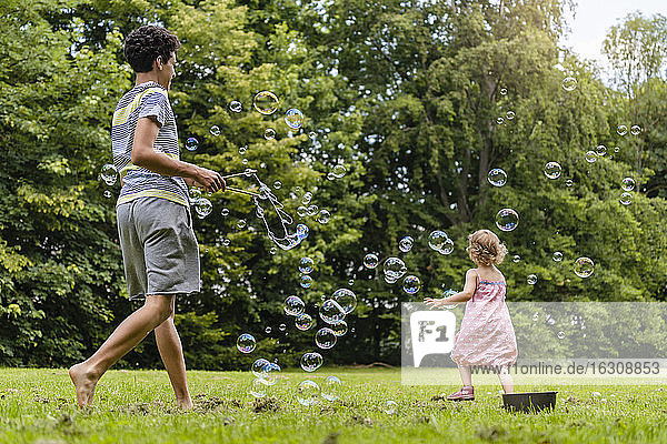 Bruder und Schwester spielen mit Seifenblasen im Park