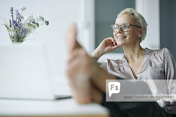 Nachdenkliche Geschäftsfrau mit hochgelegten Füßen auf dem Schreibtisch beim Entspannen im Büro