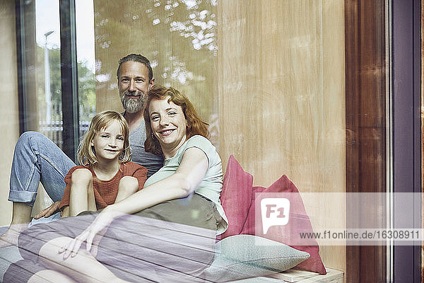 Lächelnde Familie  die sich zu Hause auf dem Bett entspannt  gesehen durch ein Fenster