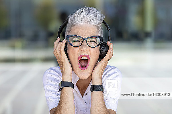 Excited senior woman screaming while listening to music through headphones
