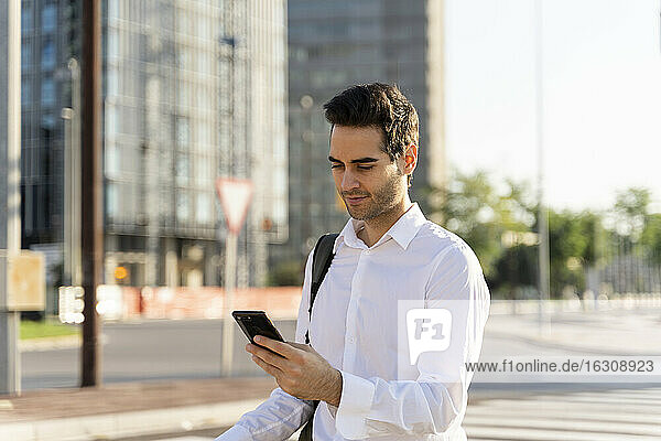 Businessman using smart phone while standing on street in city
