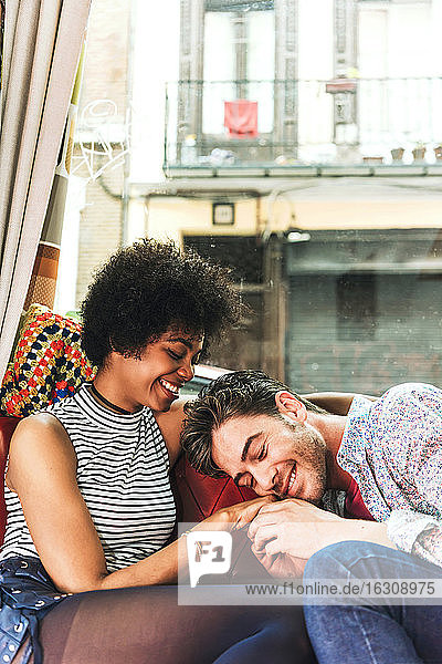 Lächelnder Mann mit geschlossenen Augen hält die Hand seiner Freundin  während er in einem Café am Fenster sitzt