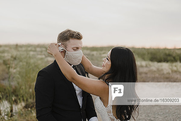 Die Braut bedeckt das Gesicht des Bräutigams mit einer Schutzmaske während COVID-19