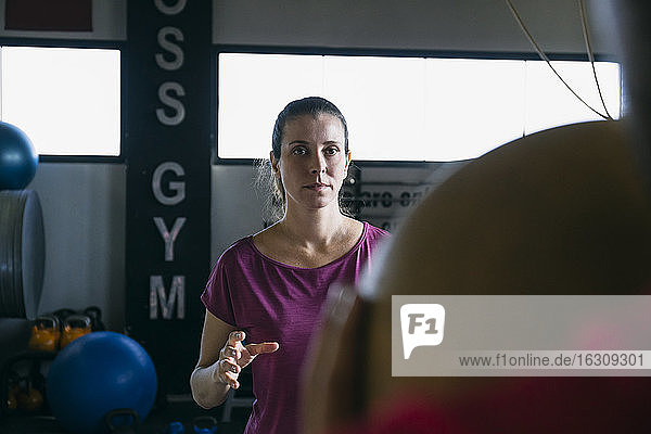 Fitness-Instruktor wirft Ball in Richtung Frau  während er mit ihr im Fitnessstudio trainiert