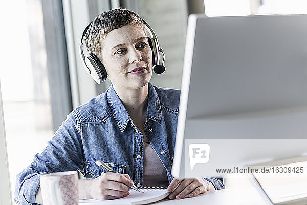 Geschäftsfrau mit Headset am Schreibtisch im Büro macht sich Notizen