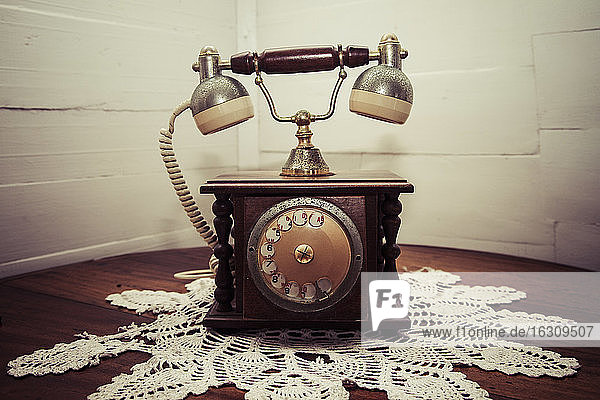 Altes Telefon auf gehäkelter Tischdecke in einer Ecke stehend