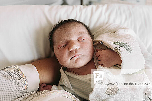 Nahaufnahme eines neugeborenen Mädchens  das auf dem Arm der Mutter im Krankenhaus schläft