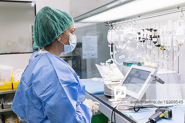 Weibliche Wissenschaftlerin betrachtet Infusionstropfen  die auf einem Gestell im Labor hängen