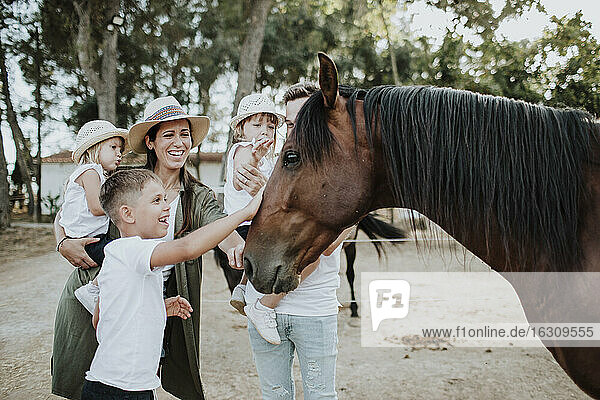Fröhliche Eltern mit Kindern  die ein Pferd berühren  während sie im Freien stehen