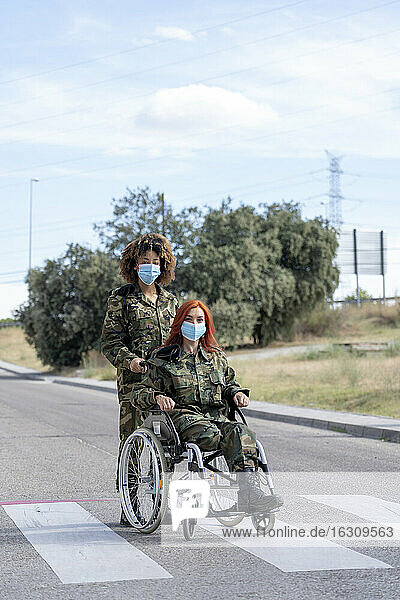 Eine Soldatin hilft einem im Rollstuhl sitzenden Offizier  während sie eine Gesichtsschutzmaske trägt.