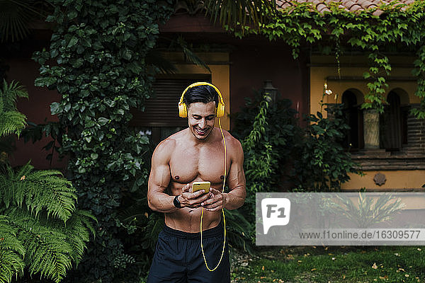 Hemdloser Mann im mittleren Erwachsenenalter hört Musik über Kopfhörer  während er im Hof steht