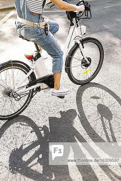Low section of woman riding bicycle on street during sunny day