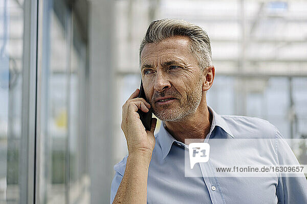 Close-up of male professional talking over smart phone in greenhouse