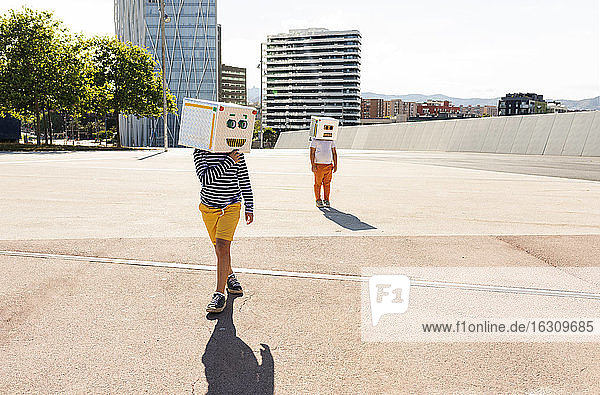 Boys wearing robot masks posing on road in city during sunny day