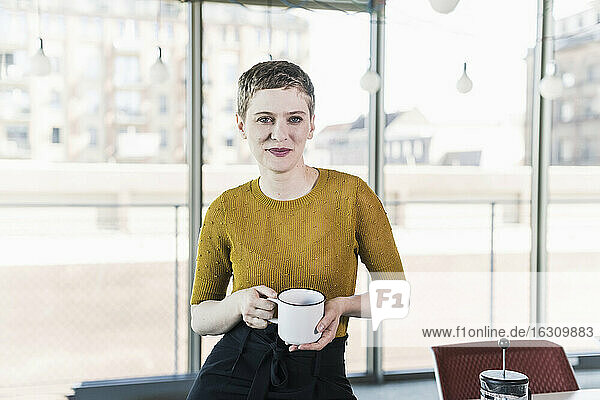 Porträt einer lächelnden Geschäftsfrau im Büro  die einen Kaffeebecher hält