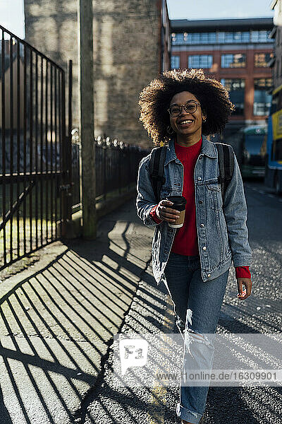 Afro young woman with coffee cup walking on street in city