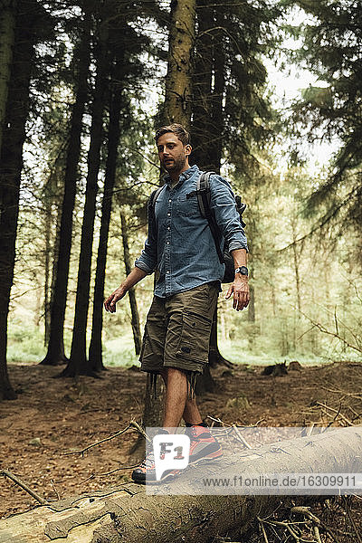 Mid adult man walking on log against trees in forest