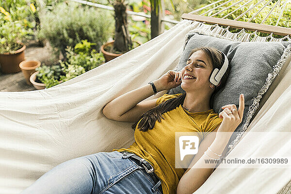 Frau mit geschlossenen Augen hört Musik über Kopfhörer  während sie sich in einer Hängematte im Garten entspannt