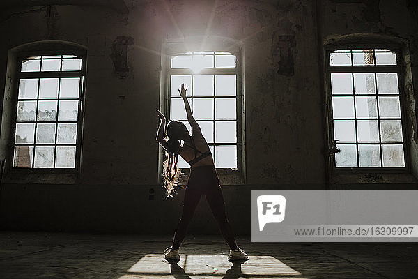Silhouette of woman exercising while standing at abandoned factory