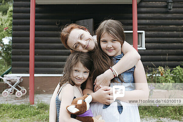 Happy mother with daughters at back yard against house
