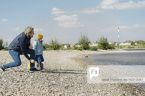 Vater und Tochter betrachten den Fluss  während sie in der Nähe des Ufers einen Kieselstein ins Wasser werfen